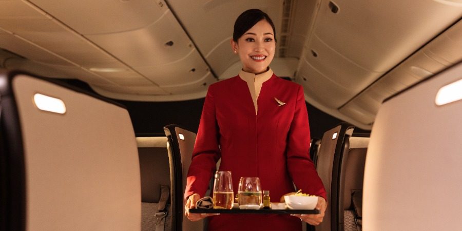A Cathay Pacific cabin crew member smiles while carrying a meal tray in the cabin.